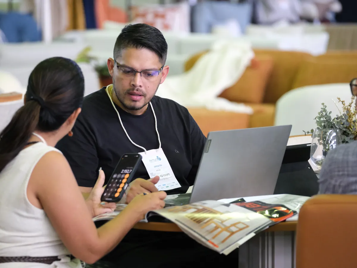Lojista e expositora acertam um pedido no notebook, à mesa do estande